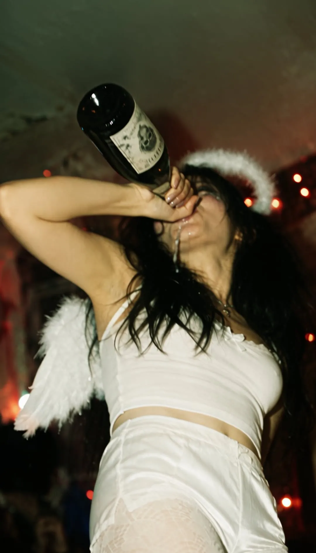 Chica con halo de ángel y pantis AIRE bebiendo en una fiesta de Halloween